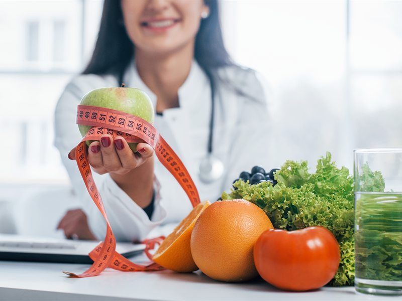 Nutrióloga en consulta con fruta fresca, verduras y cinta métrica